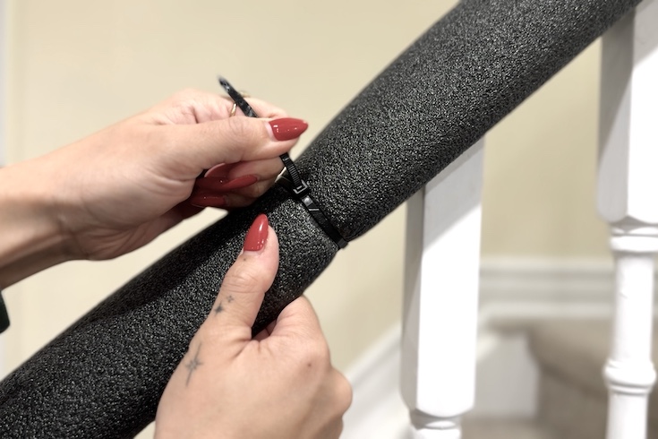 Zip tie the pool noodle to the bannister