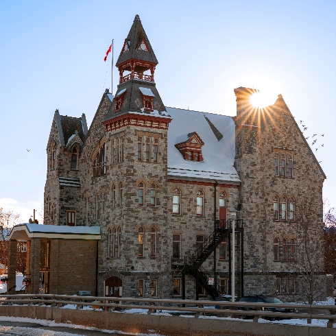 Almonte, Ontario's town hall in winter topped with snow and the sun shining behind it.