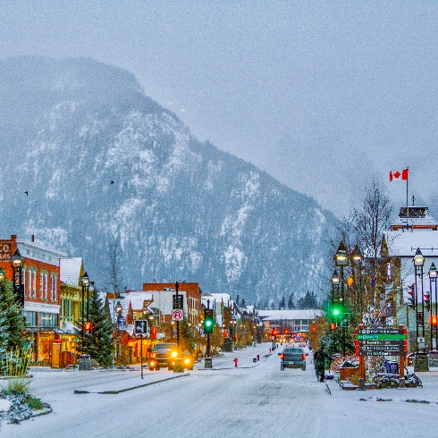 A street in Banff, Alberta with colourful buildings, decorated trees and snowy mountain backdrop.