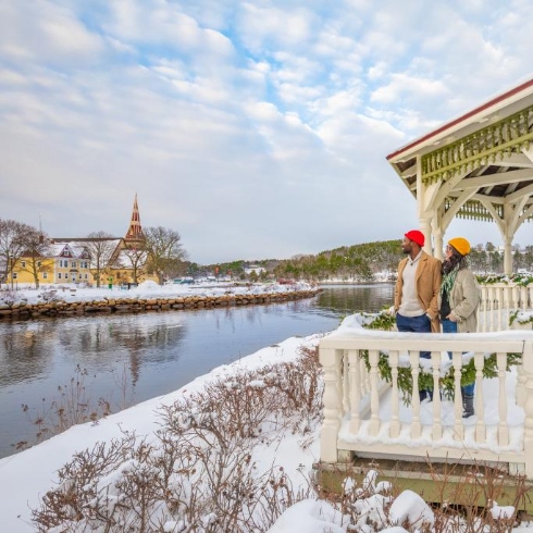 A snowy Mahone Bay, Nova Scotia with a couple looking out at the water from a white gazebo.