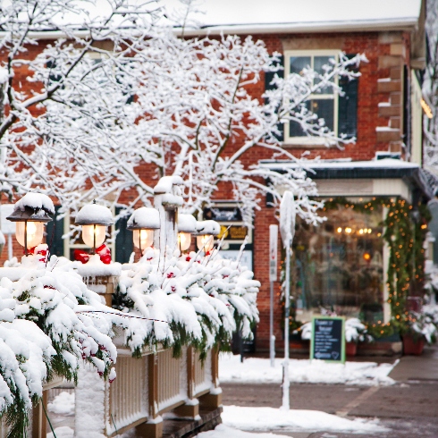 A wintery Queen Street in Niagara-on-the-Lake, Ontario with red buildings and snow-covered trees.