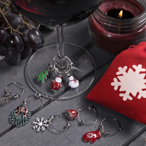 Dainty holiday-themed wine charms are placed at the bottom of a wine glass and on the top of a table.