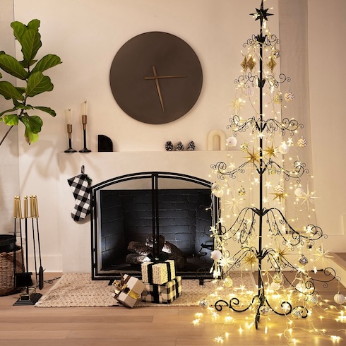 A black decorative metal Christmas tree covered in lights, sitting in front of a sleek fireplace. Check-patterned gifts sit on the floor nearby.