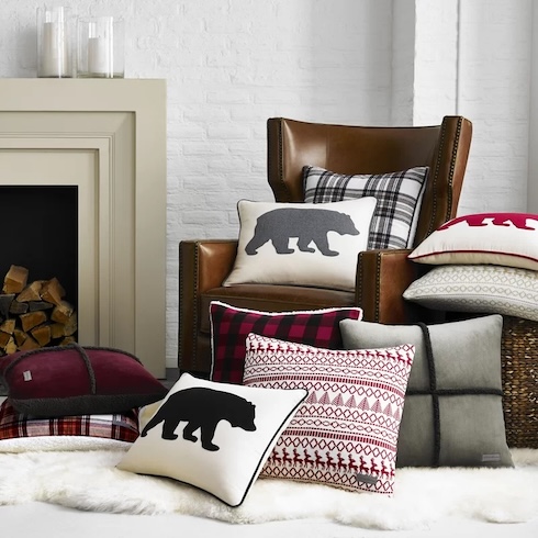 An array of cozy patterned pillows sit on a brown leather chair in front of a fireplace.