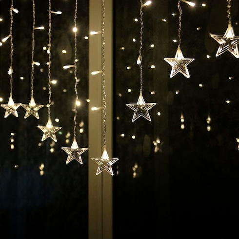 Many strings of delicate lights with stars at the ends hang in front of a dark window.