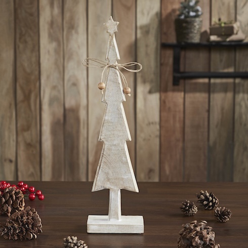 A small rustic wood Christmas tree figurine sits on a wood table that's covered in pine cones.