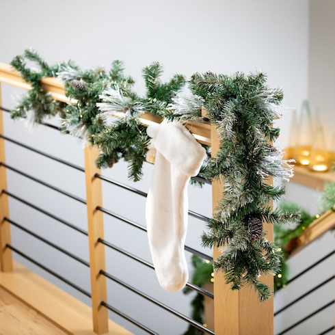 Green garland and a white Christmas stocking on a modern wood-and-metal banister in a white stairway.