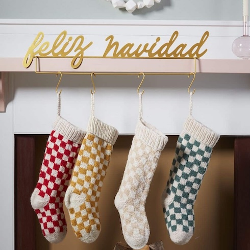 Four knit stockings in checkered patterns hang from a white fireplace mantle. A sign saying 