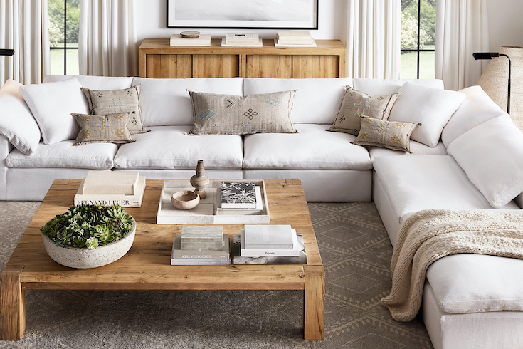 Restoration Hardware Reclaimed Oak Parsons Coffee Table sits in a bright modern living room with a huge white sectional couch and a wooden credenza for a Home Network post on how to style a coffee table