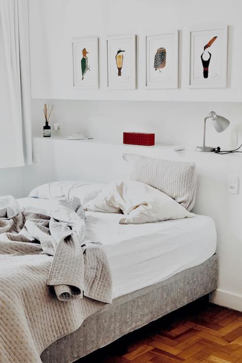 Lovely white bedroom with an unmade bed, recessed shelf and white framed bird prints