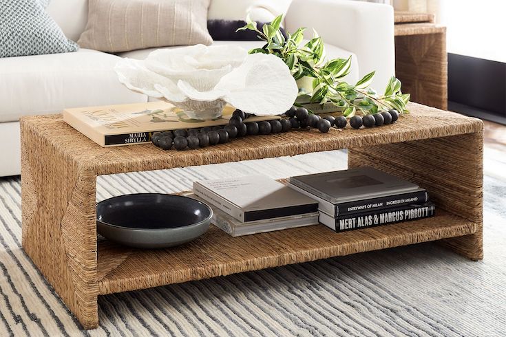 Pottery Barn Malibu Rectangular Woven Coffee Table styled with coffee table books, bowls, a piece of coral, large beads, and a potted vine