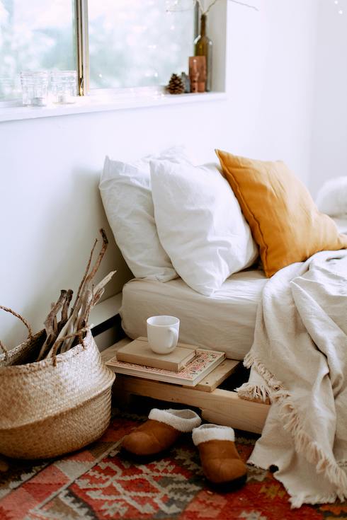 A lovely bedroom with a floor bed, rumpled linens and pillows, red rug, woven basket, and slippers next to the bed for 10 Hidden Spots That Need a Deep Clean in Your Bedroom on Home Network