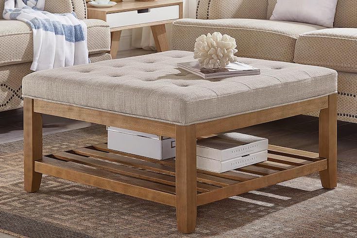 Large Square Upholstered Tufted Linen Ottoman Coffee Table on Amazon with white boxes on its lower wooden shelf and book and piece of coral perched on top