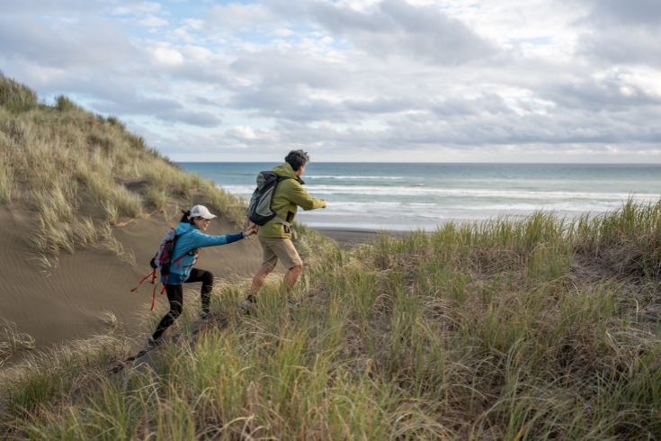 Couple helping each other on a coast hike at Muriwai Beach, New Zealand