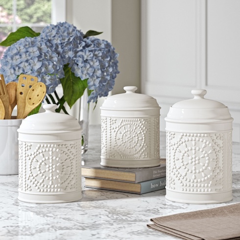 Three decorative white canisters arranged on a kitchen counter