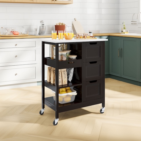 A sleek black kitchen island with a jug of juice on the top and assorted containers, bags, and a bowl of fruit on the shelves underneath.