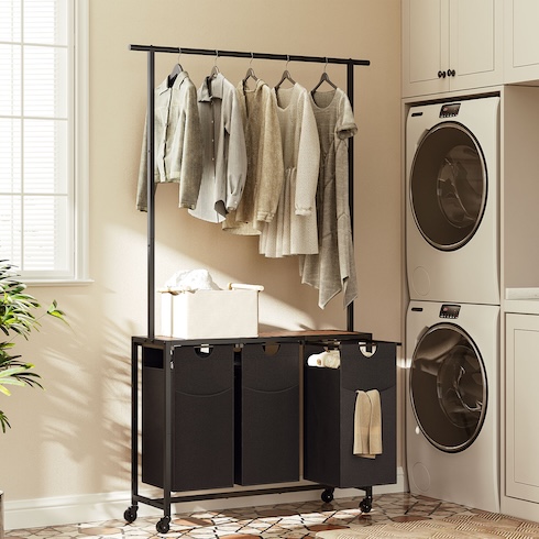 An assortment of clothes hang from hangers on a sleek laundry sorter rack in a laundry room.