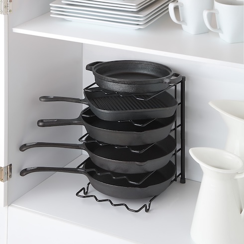 Four black frying pans are stacked on a black pan organizer