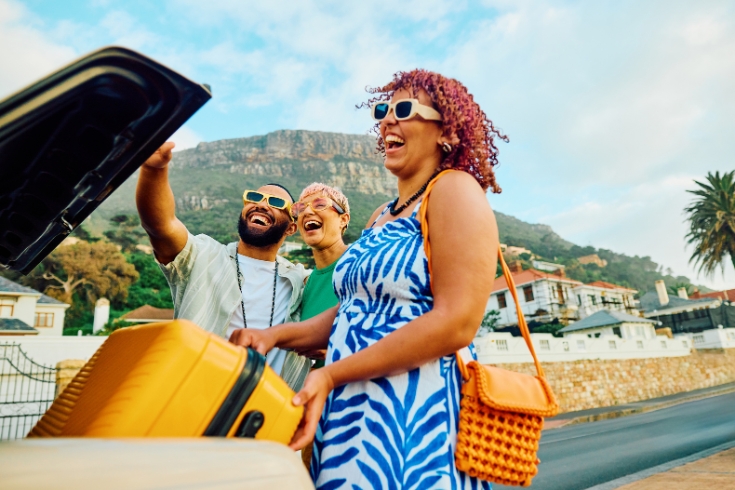 Three friends taking suitcases from the car trunk with big smiles on their faces.
