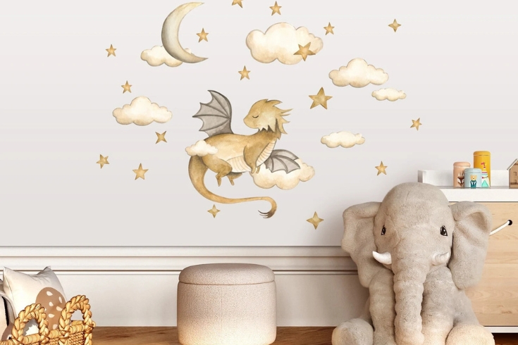 Etsy wall decal featuring a gold dragon surrounded by clouds stars and moon on a wall in a kids room with a stool and an elephant stuffie.