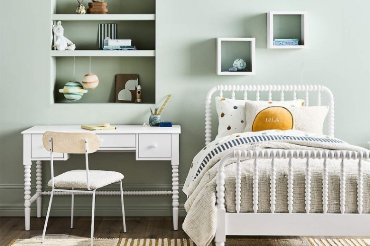 Jenny Lind White Twin Bed by Crate & Kids featured beside a study desk and chair shown in a cozy kids room against a mint green wall.
