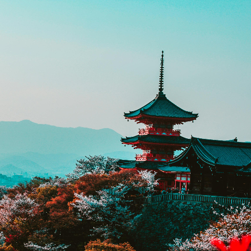 A red and black temple on a hillside with blooming trees in Kyoto, Japan with mountains in the background.