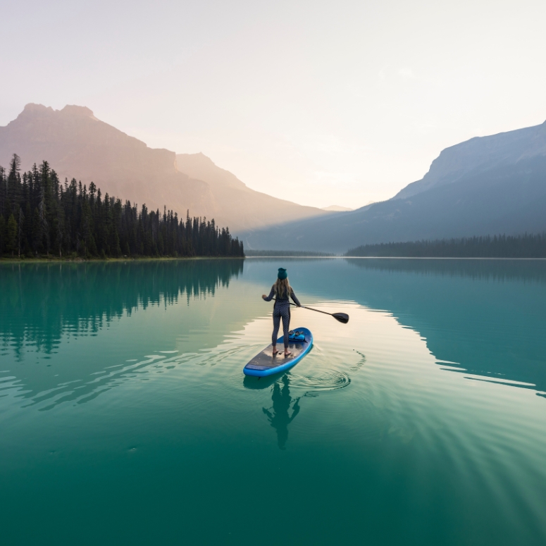 A woman paddle boarding on a beautiful blue lake surrounded by nature in Yoho National Park.