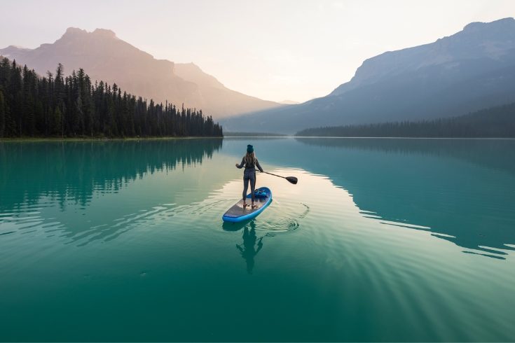 A woman paddle boarding on a beautiful blue lake surrounded by nature in Yoho National Park.