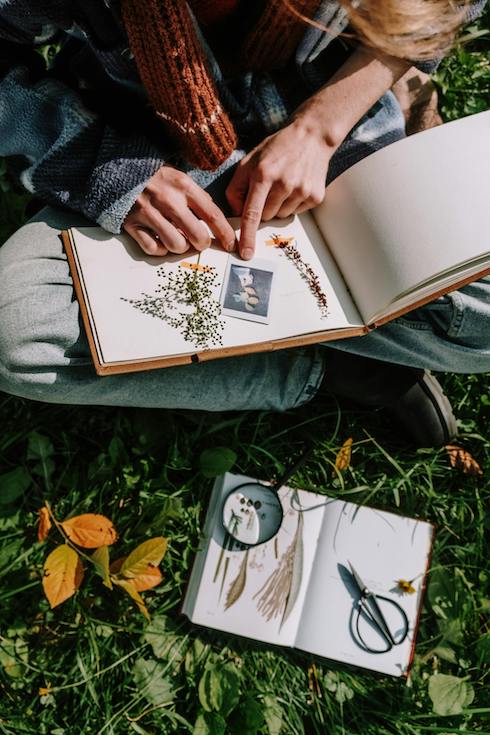Woman sitting in grass, picking flowers and sticking them into a journal