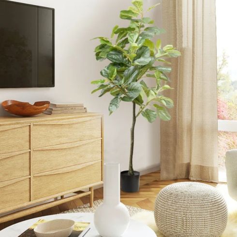 An artificial gif plant placed beside a TV and wooden cabinet.