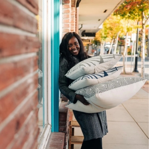 Linda Adimora, founder of Batiqua, smiling while holding pillows from her brand