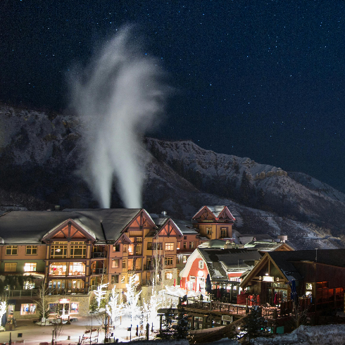 Aspen Snowmass Ski Resort at night with lit up buildings and snow making machines at work.