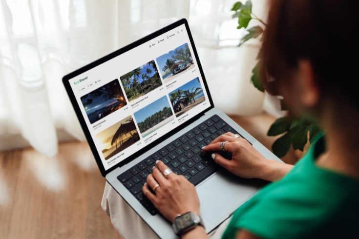 Woman using laptop showing online travel booking platform with various hotels. 