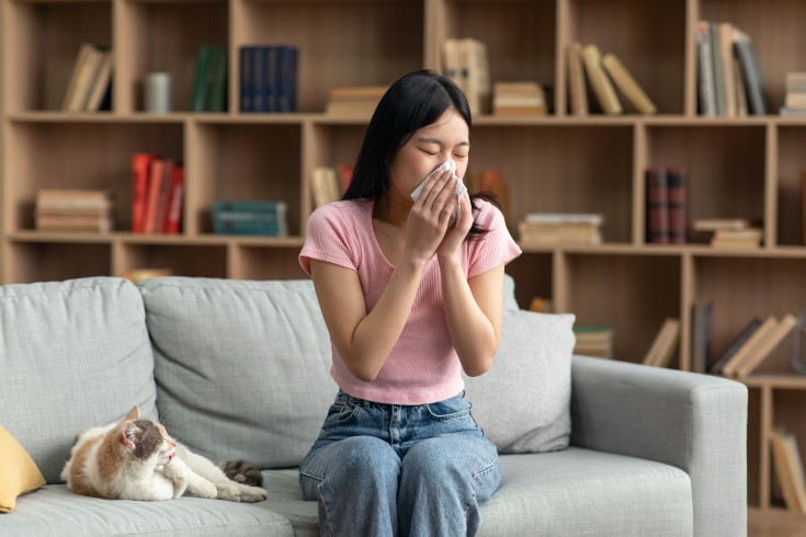 woman sneezing beside a cat