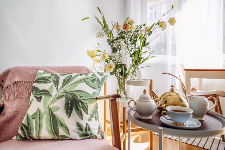 Dainty flower arrangement set beside a pink couch and table with teapot.