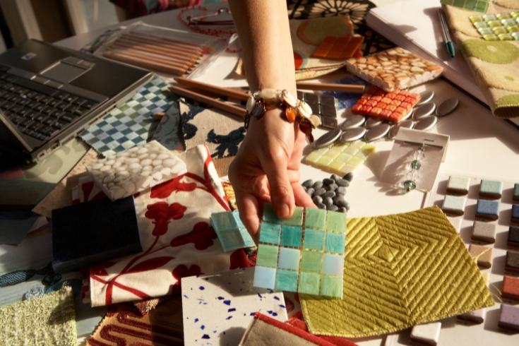 A hand picking up a blue and green pattern swatch among many others scattered on the table