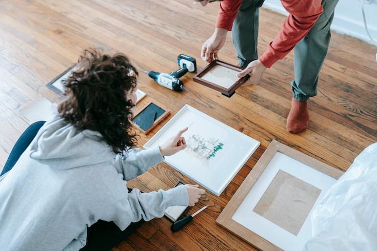 Couple arrange artwork on the floor in preparation of making a gallery wall