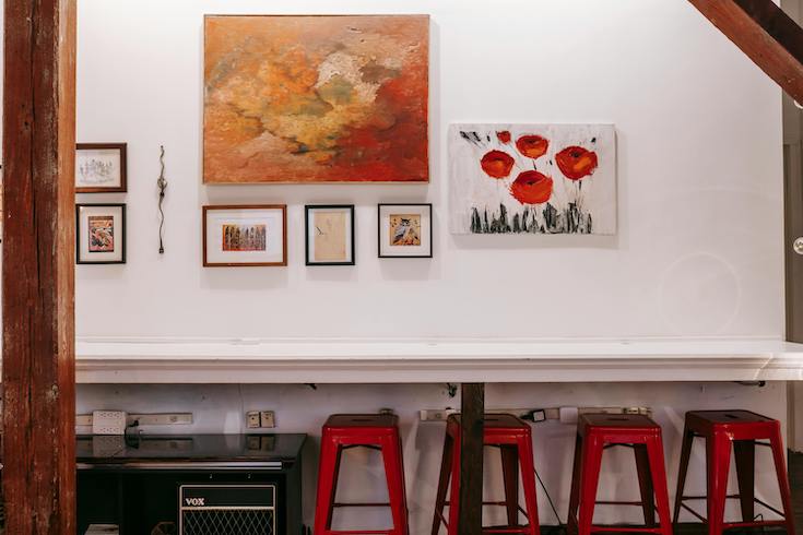 White counter with a white wall hung with framed pictures and four red stools underneath and two wooden beams on the side of the image