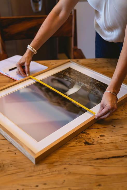 Woman's arms measuring a photo frame with a measuring tape on a wooden table