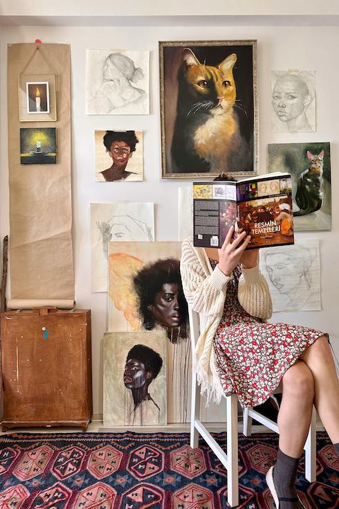 A woman sitting on chair reading a book in front of an art gallery wall in a studio as part of Home Network's Make the Perfect Gallery Wall on the First Go