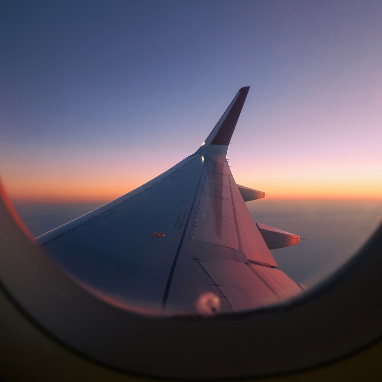 View through airplane window flight above clouds at colorful sunset.