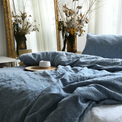 A bed covered in cozy blue linen duvet cover and pillowcase with a cup of coffee on top.