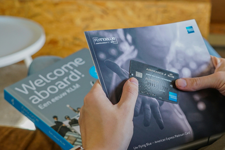A person holds up an American Express loyalty cards and a travel magazine