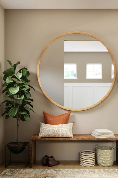 A round wall mirror with wooden frame featured with house plant and a bench.