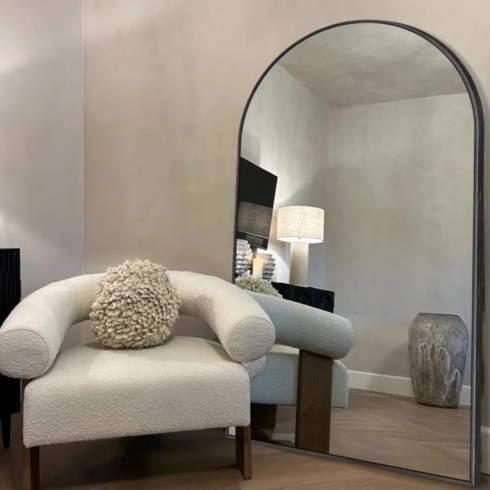 Arched full-length metal framed floor mirror beside a sofa chair.