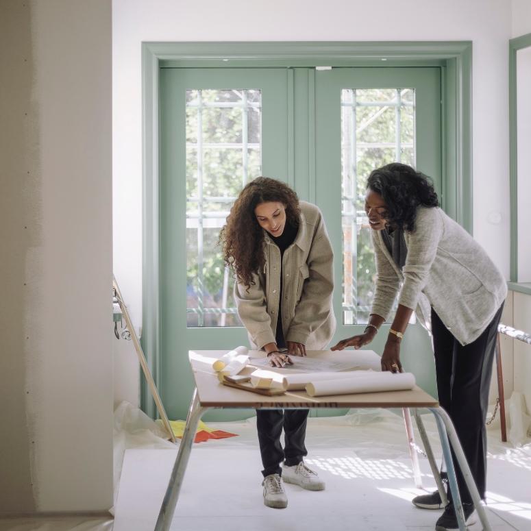 Two women discussing over blueprint with client at under construction apartment