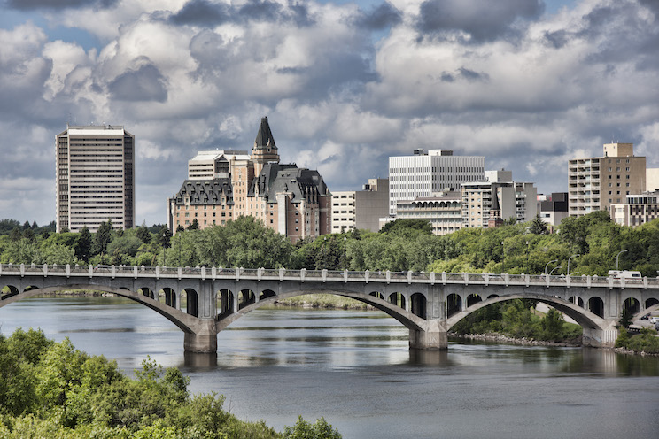 Saskatoon skyline with dramatic clouds seen from the Meewasin Trail. The University Bridge, several hotels, apartments and office buildings can be seen in the image.