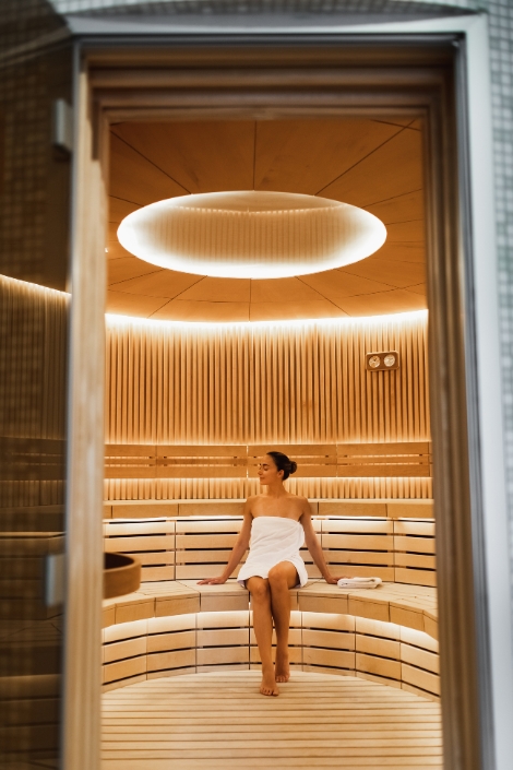 Woman in sauna relaxing in luxury interior of wooden spa cabin with dry steam. 