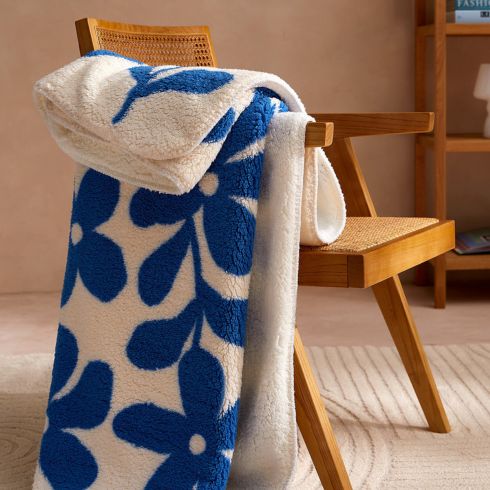 Blue and white graphic flower throw blanket on arm of wooden chair