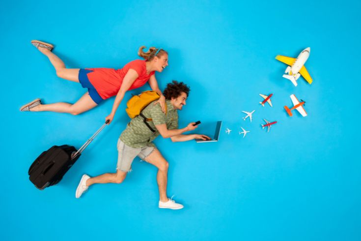 Couple with suitcase looking at laptop with airplanes coming out.